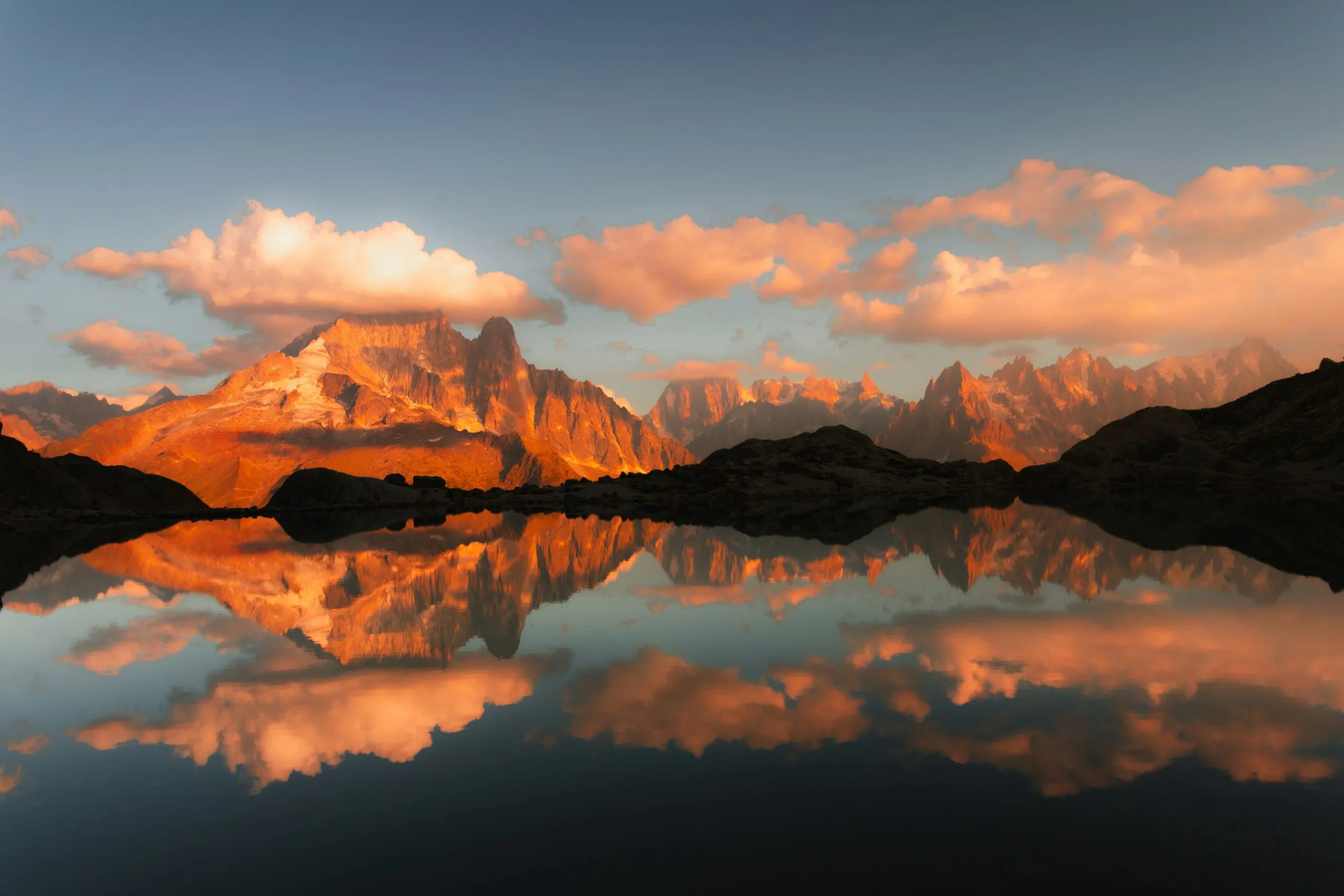 Reflet des sommets enneigés et des nuages dorés au coucher du soleil dans un lac de montagne